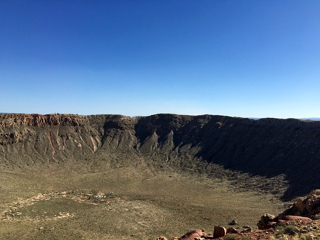 meteor crater natural landmark in the middle of a desert with a blue sky in the background.