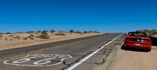 A red convertible is parked on the side of route 66 in the desert