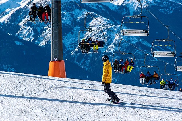A snowboarder is riding down a snow covered slope next to a ski lift.