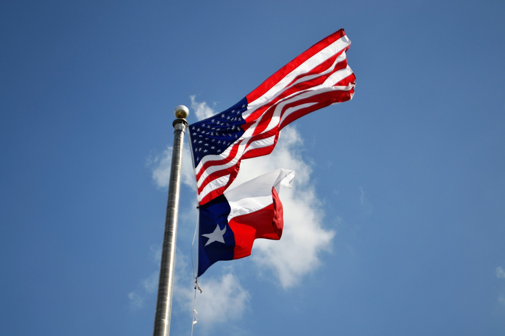 An american flag and a texas flag are waving in the wind.