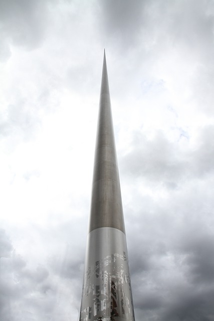 A tall metal tower known as the spire with a cloudy sky in the background.