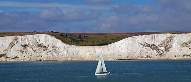 A sailboat is floating on top of the water in front of the white cliffs of Dover