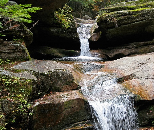 A small waterfall is surrounded by rocks in the middle of white mountain national forest