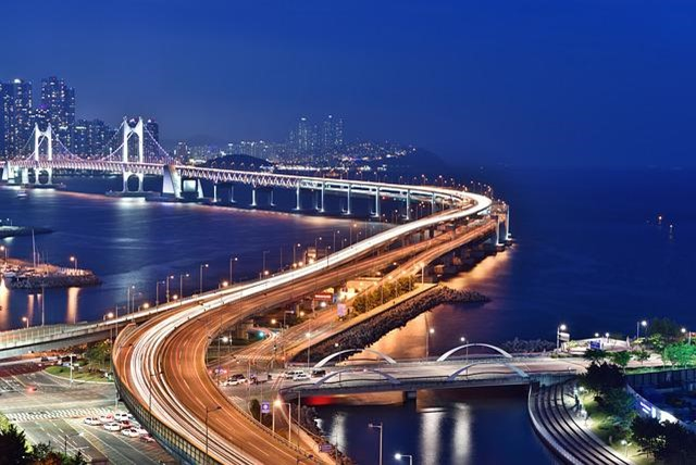 An aerial view of a bridge over a body of water in Busan at night.