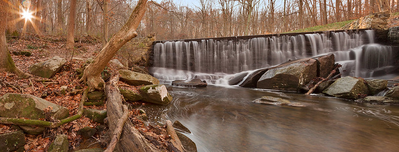 A waterfall in the middle of a Susquehanna state park with the sun shining through the trees.