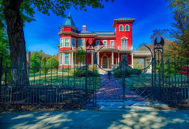 A large red house owned by Stephen King behind a wrought iron fence.