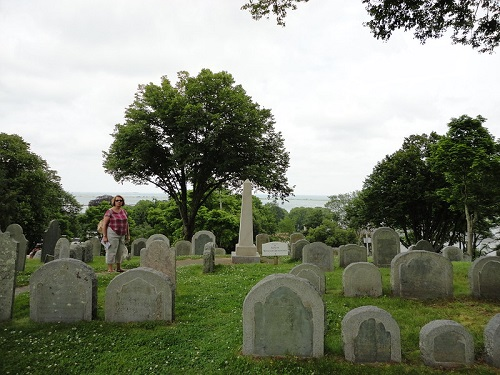 A woman is standing in a cemetery surrounded by graves and trees in Plymouth