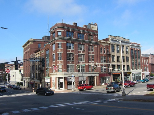 A busy intersection with a large brick building in the background in Bangor