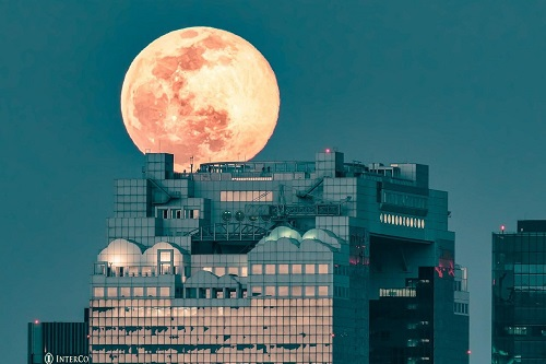 A full moon is rising over a tall building in Osaka