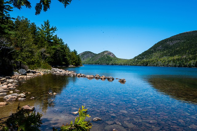 A lake surrounded by trees and rocks with mountains in the background in Acadia NP