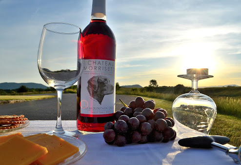 A bottle of wine is sitting on a table next to grapes and cheese.