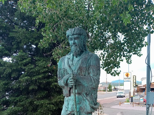 A statue of a man with a beard is standing in front of a tree.