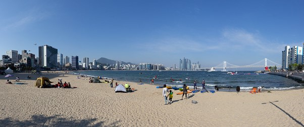 A panoramic view of a beach in Busan with a city in the background.