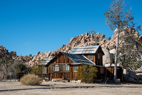 A wooden house in the middle of Joshua Tree NP with rocks in the background.