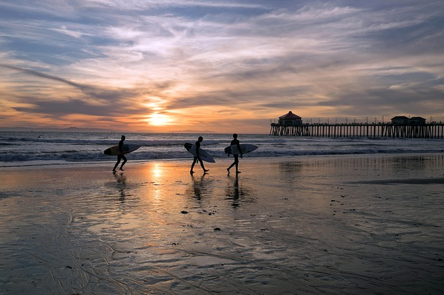 Three surfers are walking on the beach at sunset near Santa Monica pier