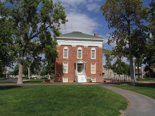 A large brick building with a green roof is surrounded by grass and trees