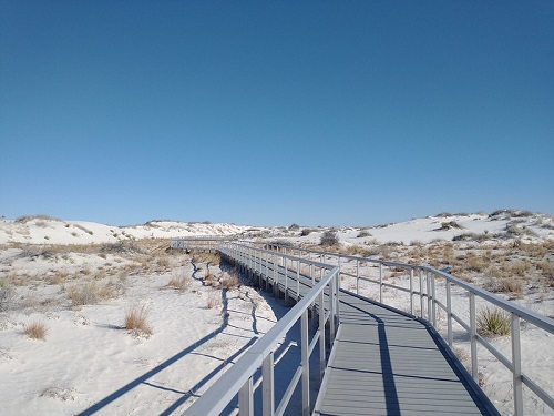 A wooden walkway leading to a sand dune in white sands national park