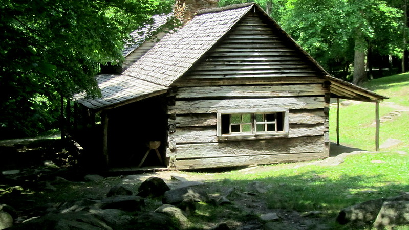 A small log cabin is sitting in the middle of a grassy field in Great Smoky Mountains NP