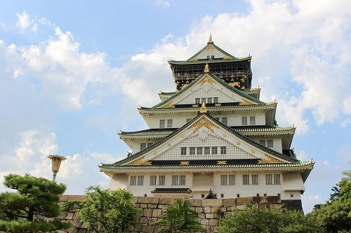 A large white building with a green roof in Osaka and a blue sky in the background.