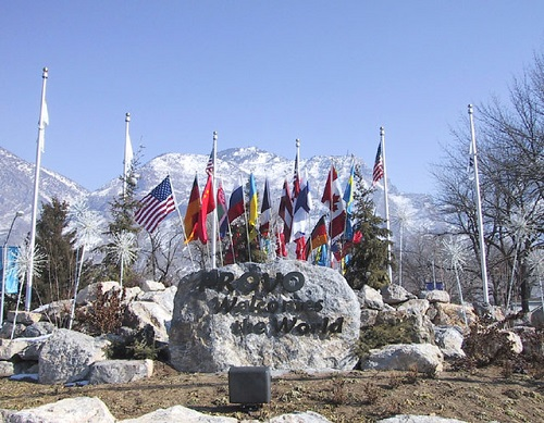 Many flags are flying in front of a large rock that says Provo welcome the world