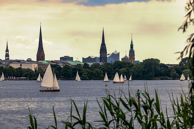 A group of sailboats are floating on a lake with Hamburg in the background.