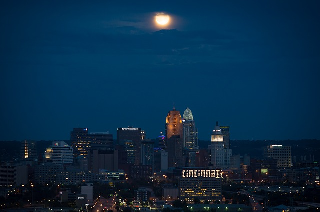 A full moon is rising over the Cincinnati skyline at night.