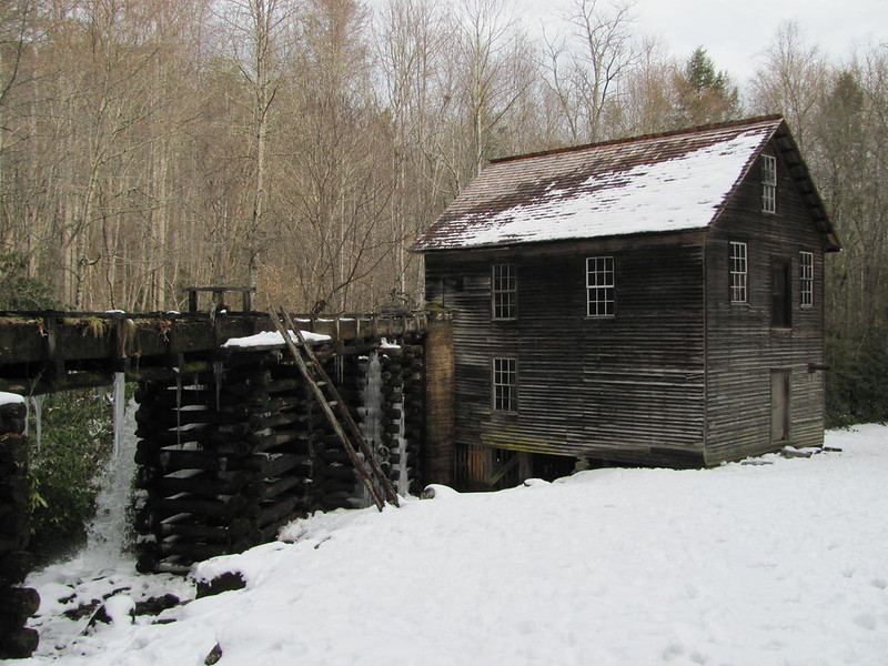 An old wooden house is surrounded by snow and trees in Great Smoky Mountains NP