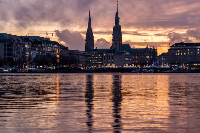 The Hamburg skyline is reflected in the water at sunset.