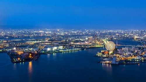 An aerial view of Osaka at night with a large body of water in the foreground.