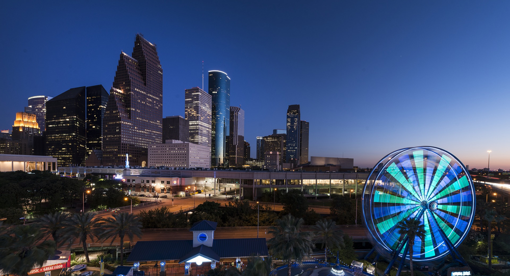 A ferris wheel is lit up in front of the houston skyline at night.