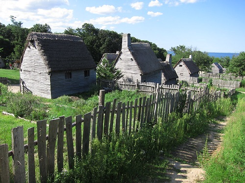 A wooden fence surrounds a row of houses with thatched roofs in Plymouth