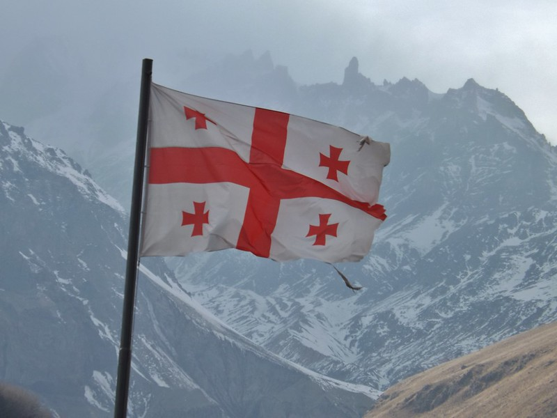 The Georgia flag flying in front of snowy mountains