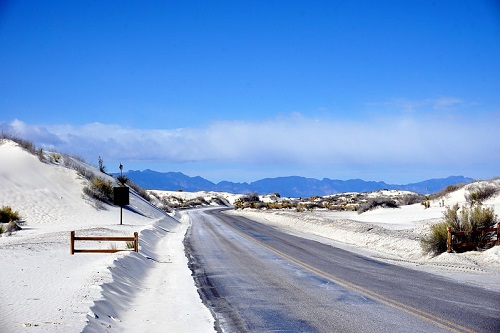 A road going through white sands national park with mountains in the background.