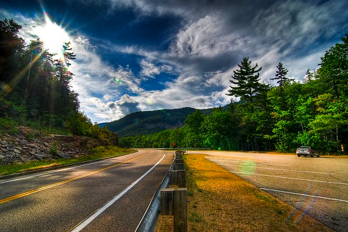 A road going through white mountain national forest with the sun shining through the clouds.