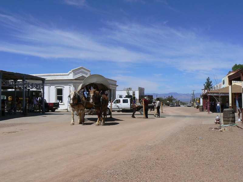 A horse drawn carriage is pulled down a dirt road in tombstone