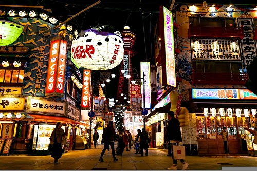 A group of people are walking down a busy Osaka street at night