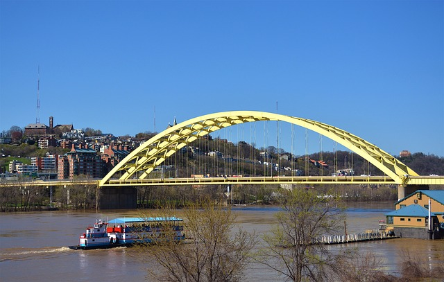 A yellow bridge over a river in Cincinnati with a boat in the water.