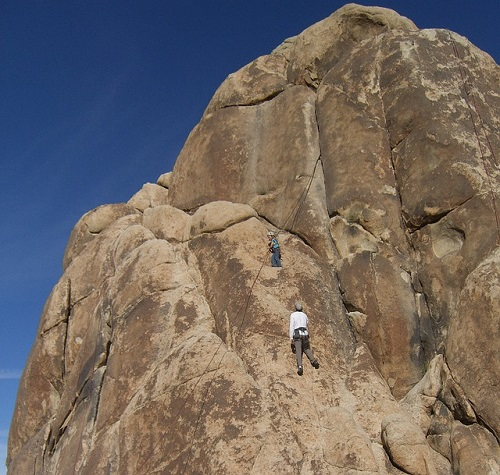 A man climbs up the side of a large rock in Joshua Tree NP