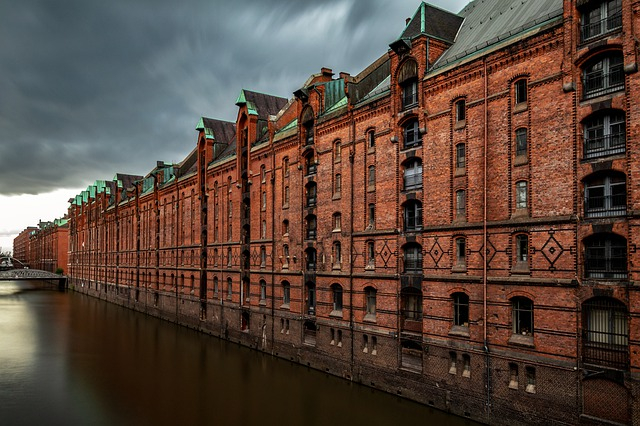 A row of brick buildings next to a river on a cloudy day in Hamburg