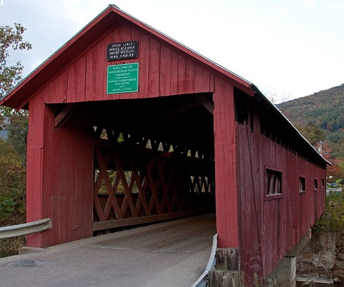 A red covered bridge with a green sign on the side