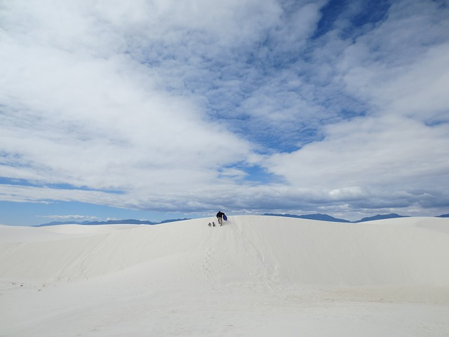 Two people are walking on top of a white sand dune in white sands national park