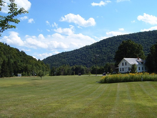 A white house sits in the middle of a lush green field in Green Mountain National Forest