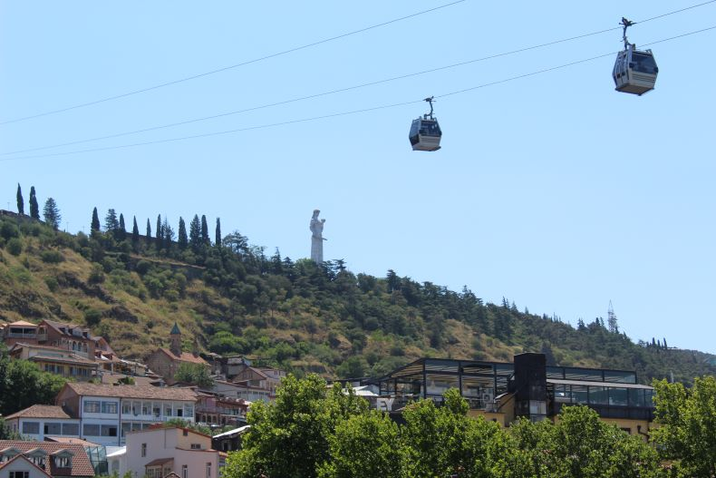 A cable car is going up a hill with a statue in the background in Georgia