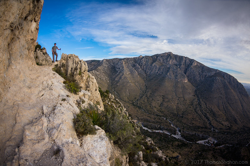 A man is standing on the edge of a cliff overlooking a mountain range in guadalupe mountains np