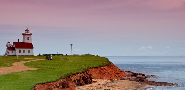 A lighthouse sits on top of a grassy hill overlooking the ocean.