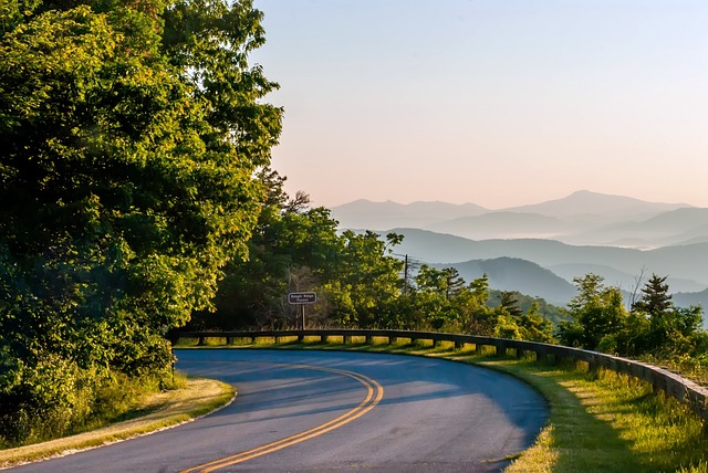 A winding road with trees on both sides and the great smoky mountains in the background.