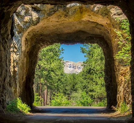 A view of Mount Rushmore through a tunnel with trees and mountains in the background