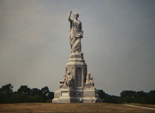 A large statue of a woman stands in the middle of a field in Plymouth