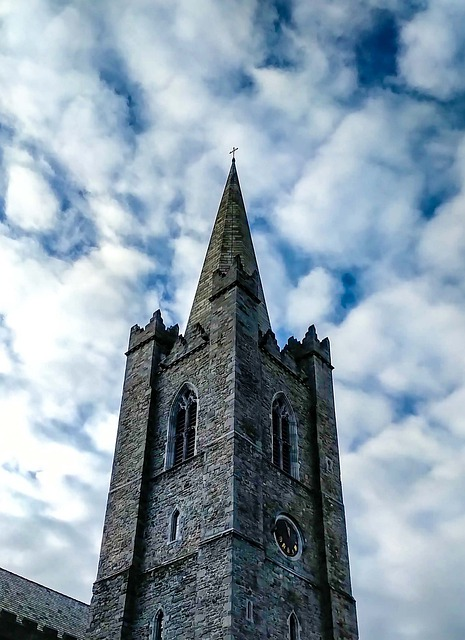 A tower on st patrick's cathedral with a clock on it against a cloudy sky.