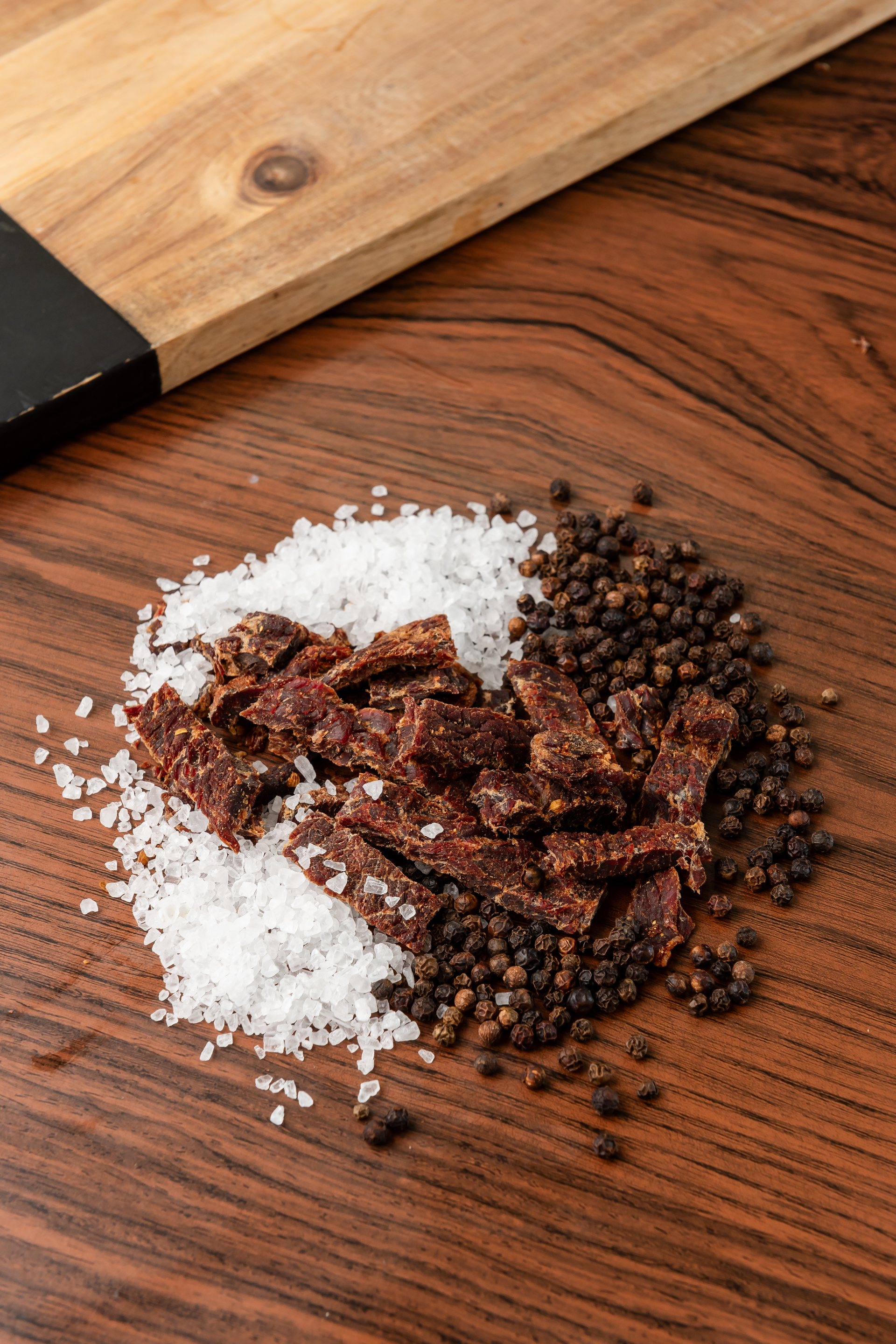 A pile of salt , pepper and beef strips on a wooden table.